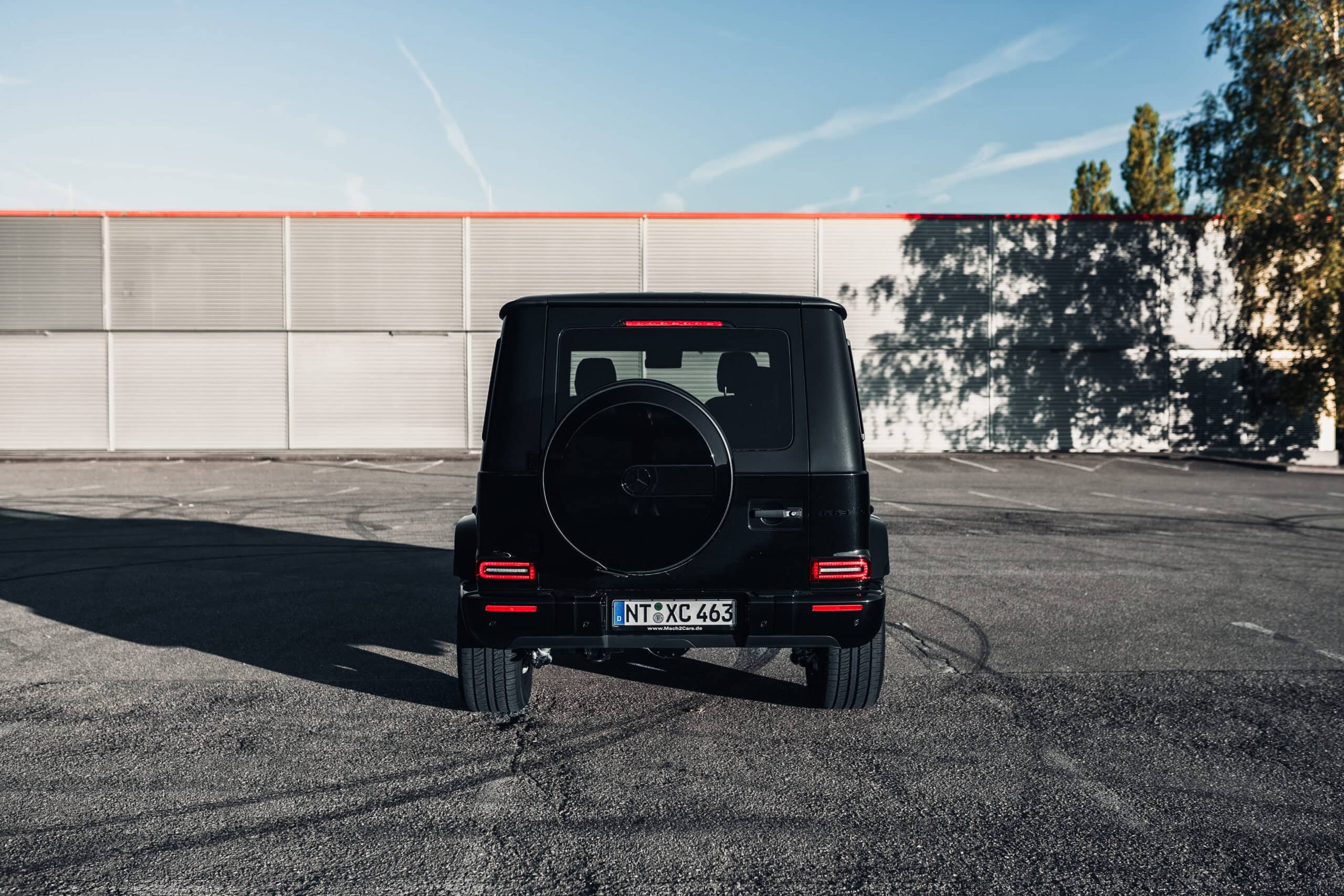 Schwarzer Geländewagen auf einem Parkplatz, sonniger Tag, moderne Architektur im Hintergrund.