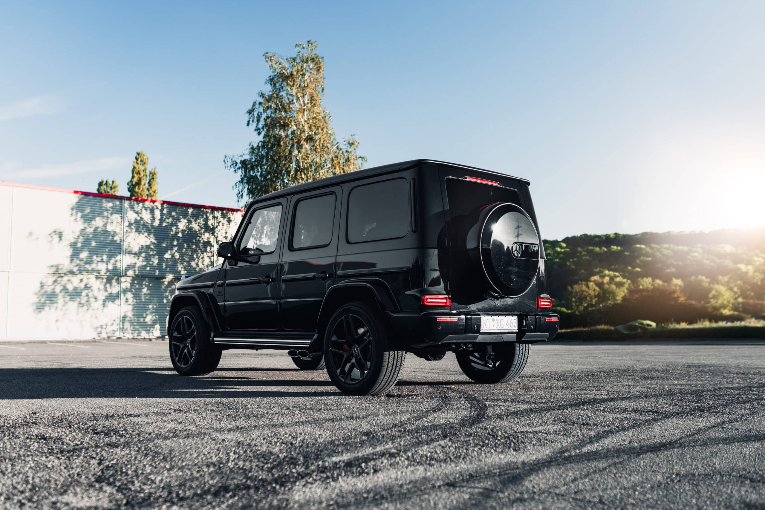 Schwarzer Geländewagen auf sonnigem Parkplatz mit Bäumen im Hintergrund.